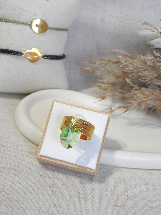 bague à anneau martelé en acier inoxydable doré, ornée d'une breloque en pierre de cristal verte. Bijou posé sur un support blanc en bambou.