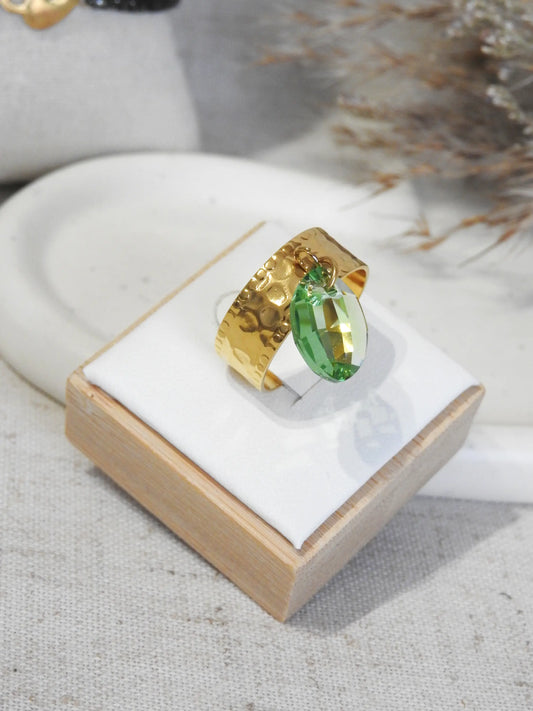 bague à anneau martelé en acier inoxydable doré, ornée d'une breloque en pierre goutte de cristal verte. Bijou posé sur un support blanc en bambou.