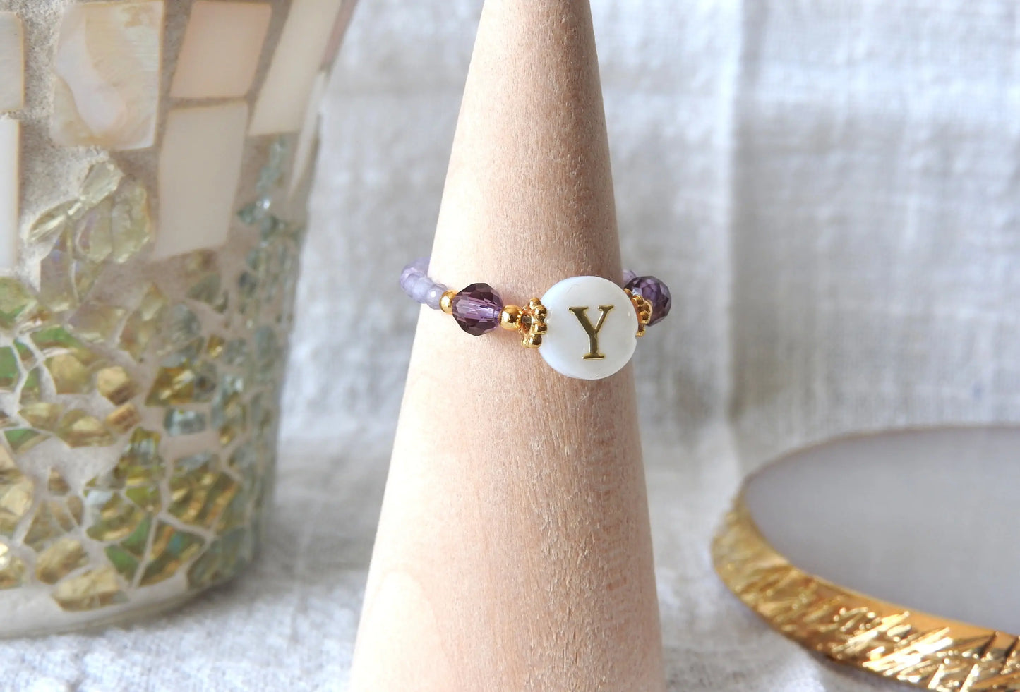 Bague élastique en perles de verre violettes et acier inoxydable doré. Bijou orné d'une perle ronde blanche avec pour motif lettre initiale y doré. Bijou présenté sur un cône bambou.