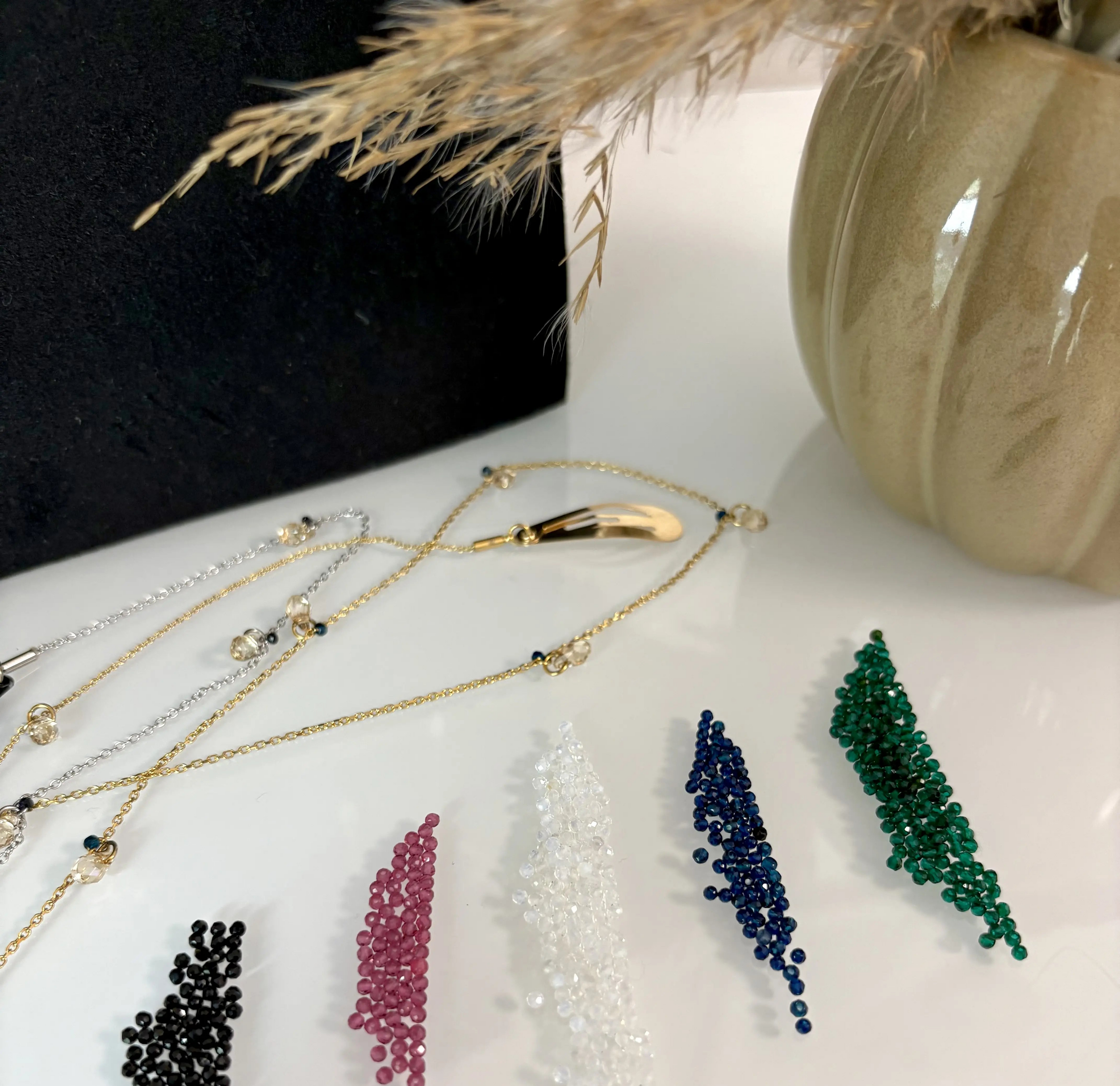 petites perles colorées noires, grenat, blanches, bleu et vertes disposées sur une table et proposée en option dans la composition d'un bijou pour cheveux, composé d'une barrette et d'une chaîne en acier inoxydable.