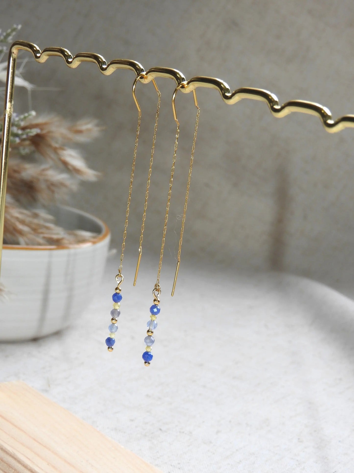boucles d'oreilles à chaînette traversante en acier inoxydable doré, suspendue sur une barre métallique doré et bambou. Bijou orné de perles de verre de tons bleus et jaune.