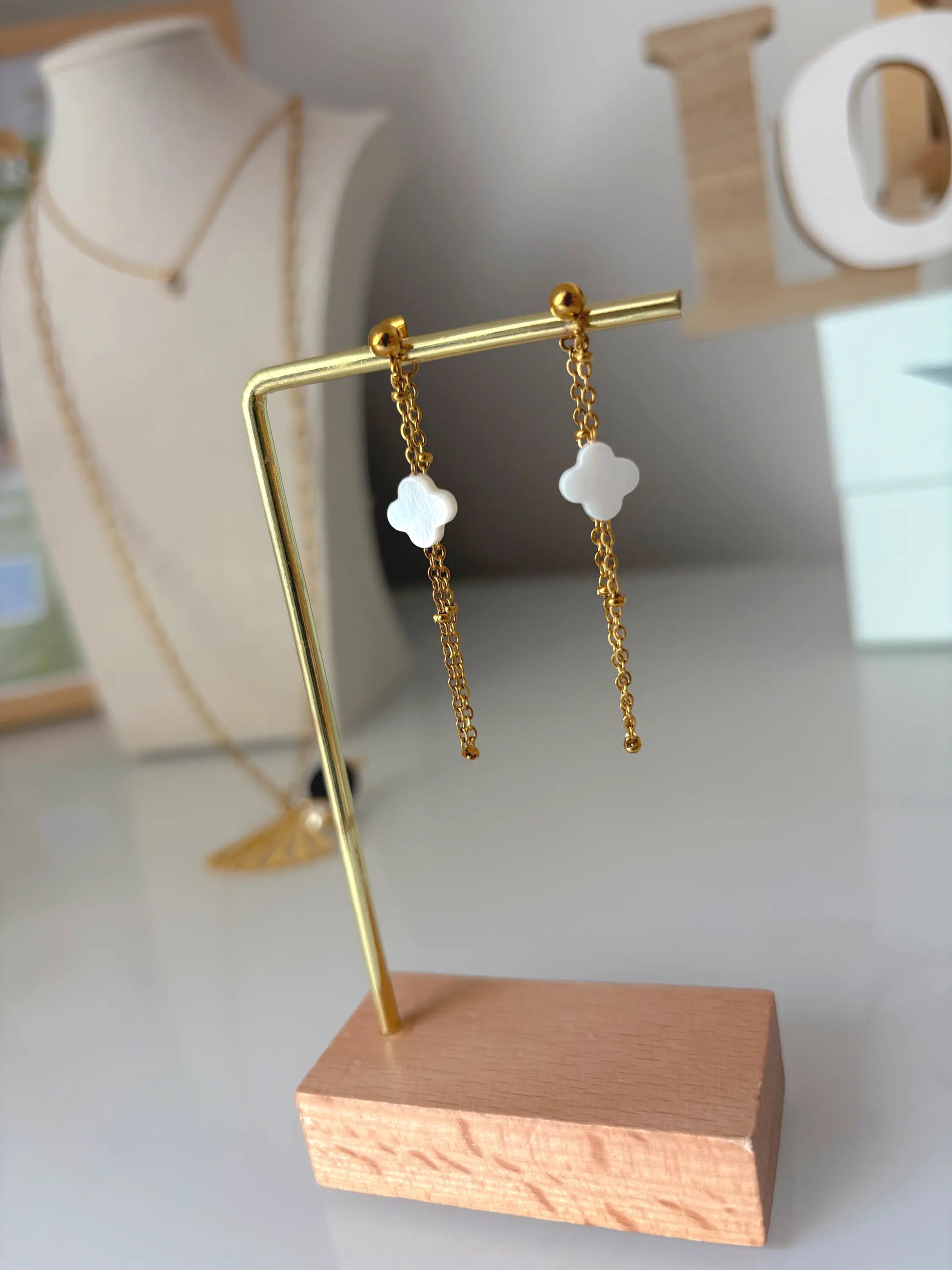 boucles d'oreilles chaînettes en acier inoxydable doré ornées d'une perle trèfle en nacre blanche. Bijou suspendu à un présentoir en métal doré et bambou.