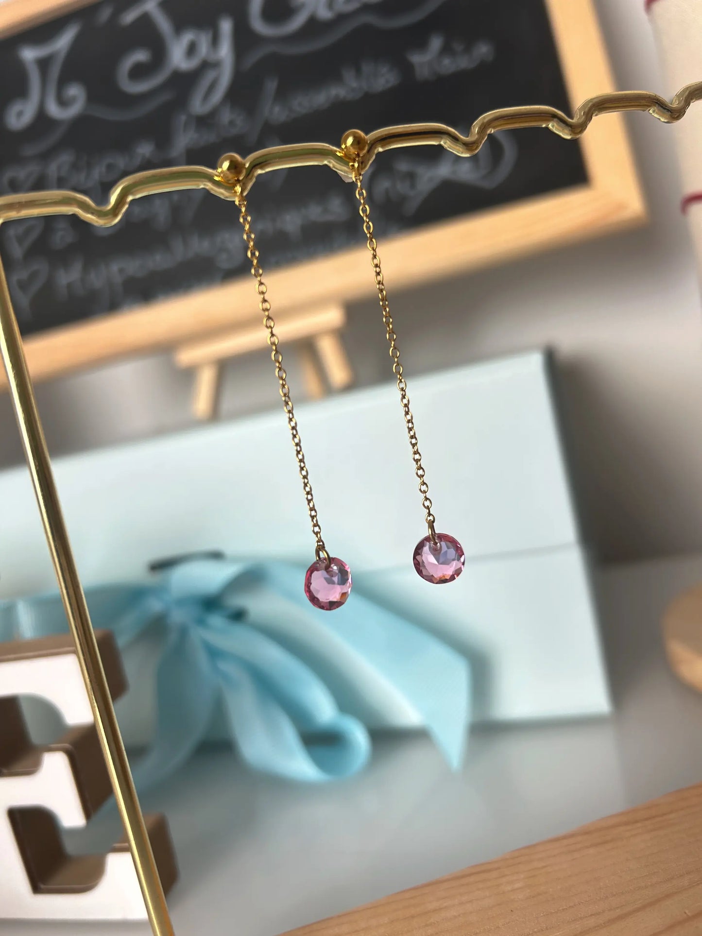 Boucles d'oreilles chaînettes en acier inoxydable doré, ornées d'une pierre en cristal rose en suspension des chaînettes. Bijou suspendu sur un support métallique doré.