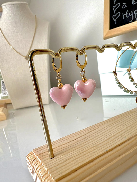 Boucles d'oreilles dormeuses créoles en acier inoxydable doré, décorées d'une perle cœur en céramique rose. Bijou suspendu sur un support métallique doré et bambou.