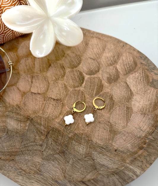 boucles d'oreilles dormeuses, mini-créoles en acier inoxydable doré et décorées d'une perle trèfle en nacre blanche. Bijou posé sur un plateau en bambou, décoré d'une pince fleur à cheveux.