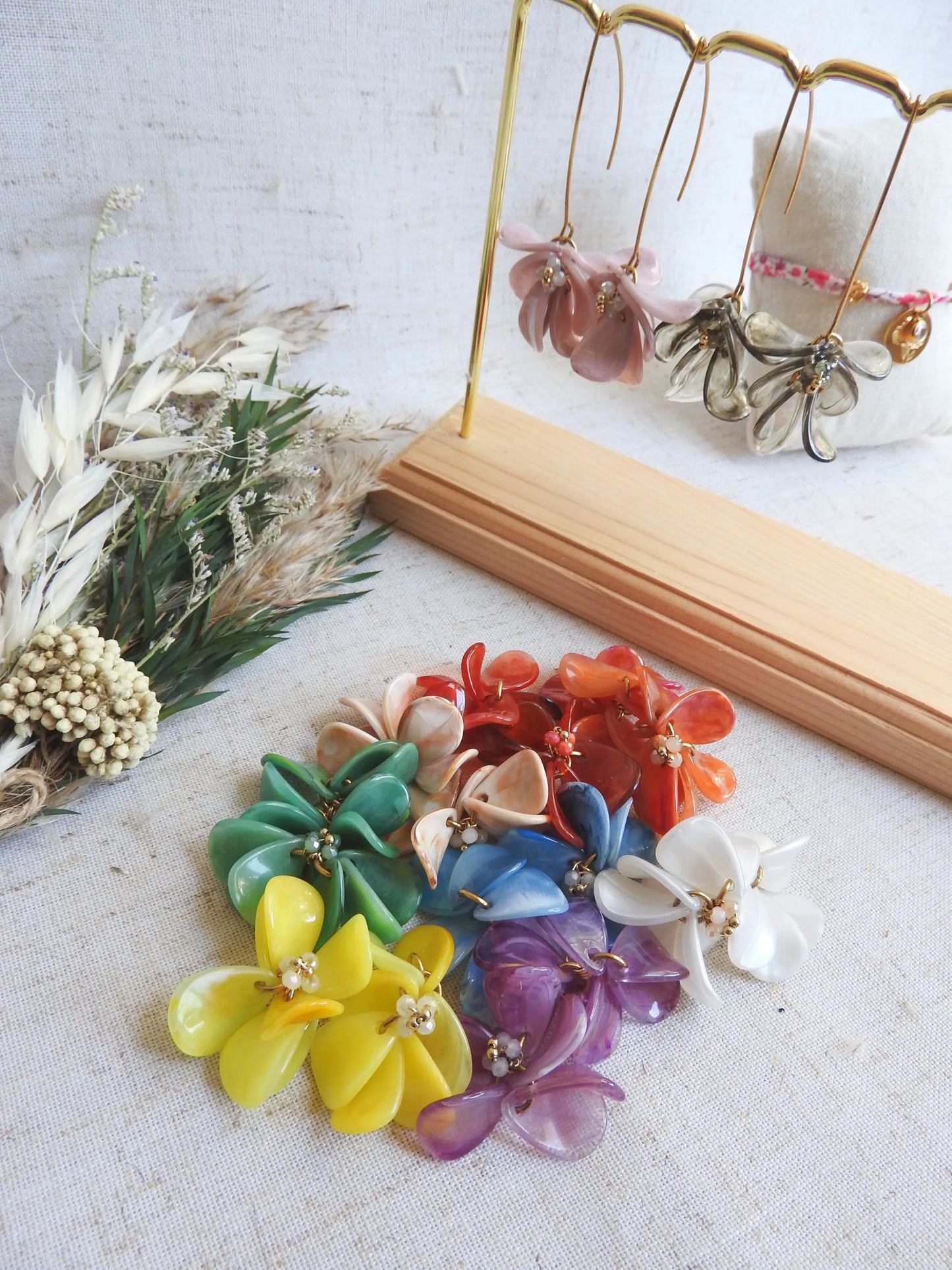 perles pétales formant différents bouquets floraux colorés : vert, beige, rouge, blanc, bleu, violet, jaune, posés à plat sur une nappe beige. Bijoux interchangeables pour les boucles d'oreilles hameçon ou créoles de la marque de bijoux M'Joy Creation.