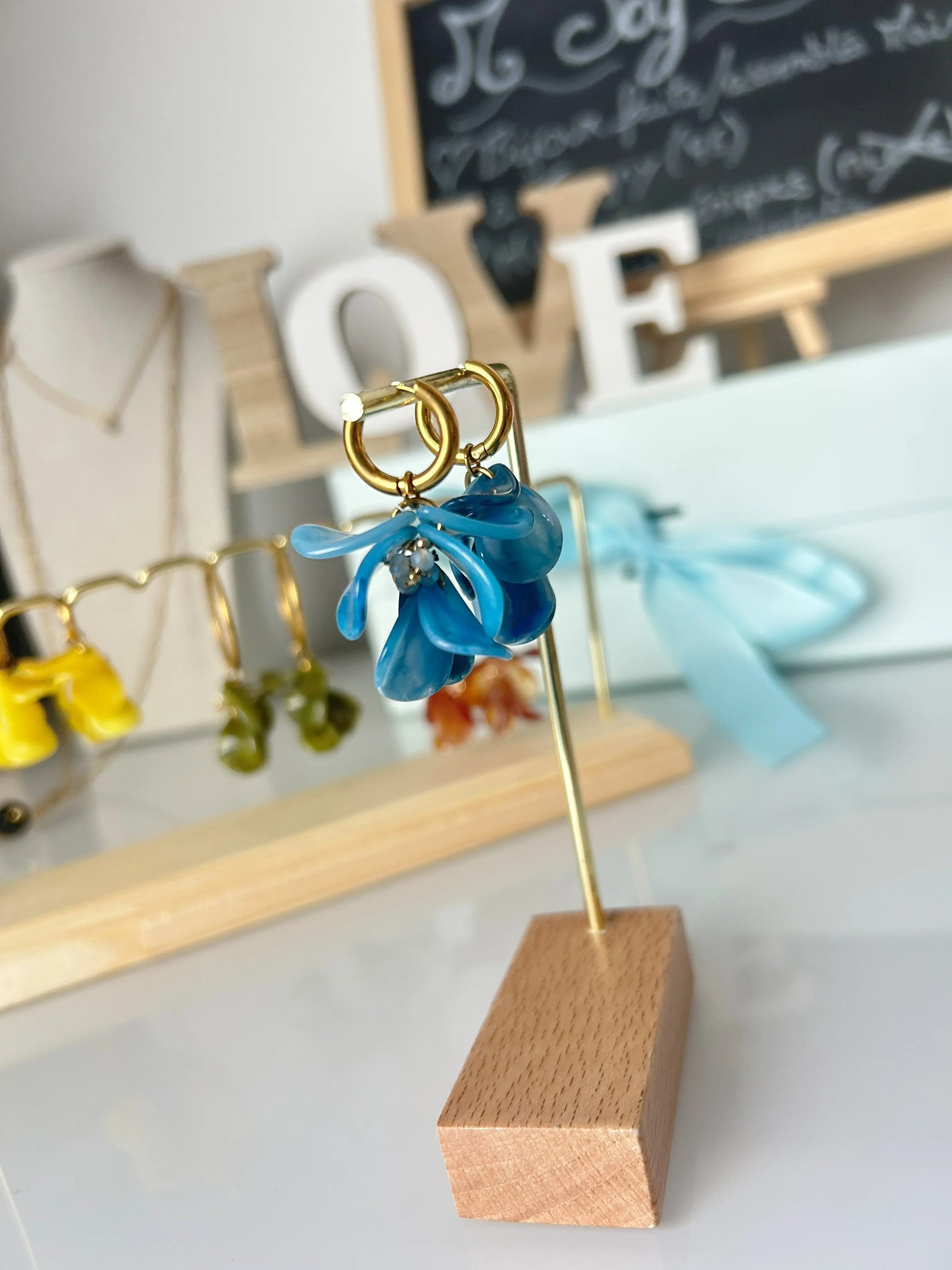boucles d'oreilles mini-créoles en acier inoxydable doré suspendues à un support pour boucles d'oreilles en métal doré et bambou. Bijou orné de pétales formant un bouquet floral en acrylique de couleur bleu.