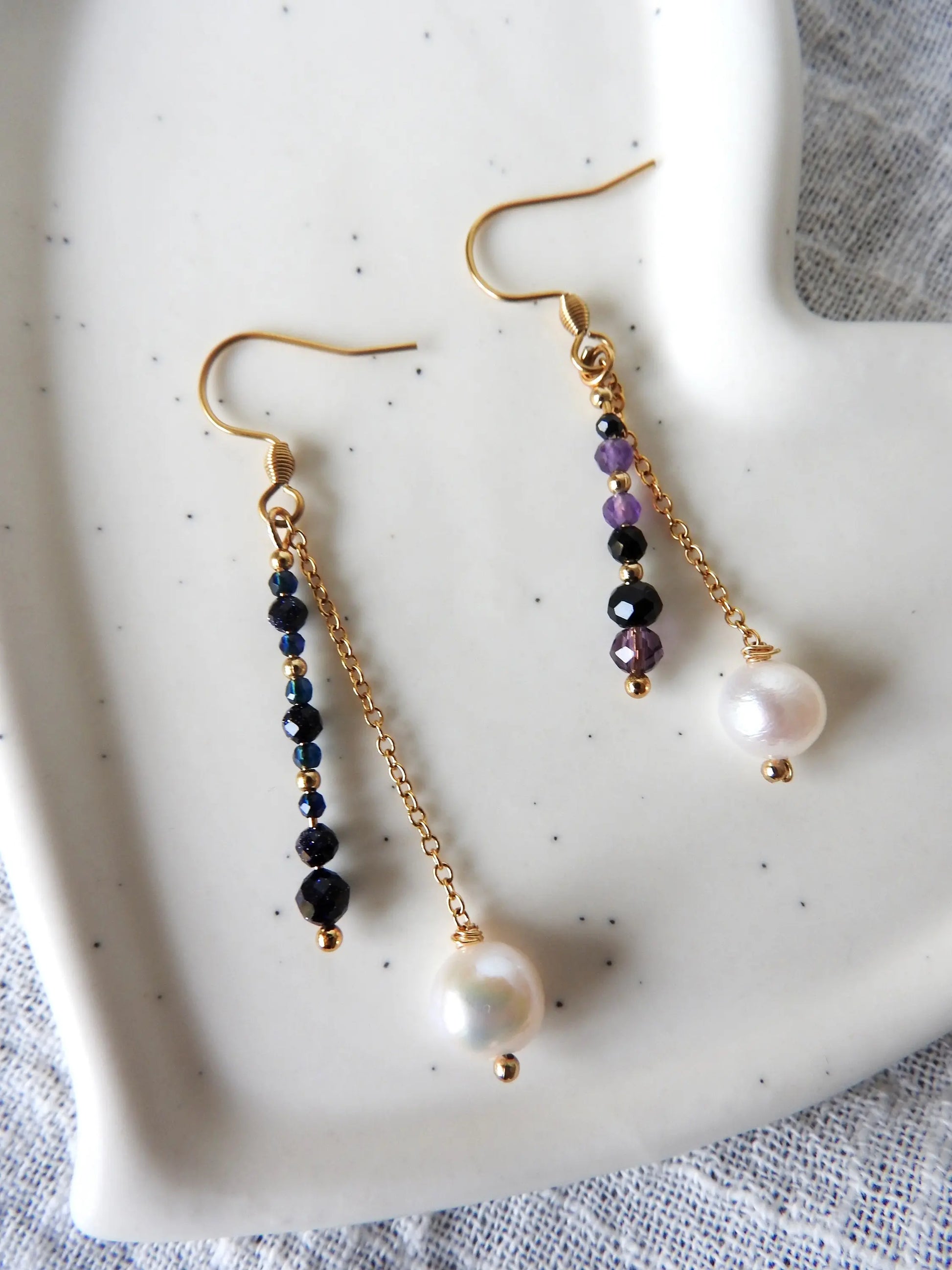 Boucles d'oreilles disposées sur une coupelle céramique blanche. Boucles duo avec barre en perles de verre colorées et perle d'eau douce suspendue à une chainette en acier inoxydable doré.