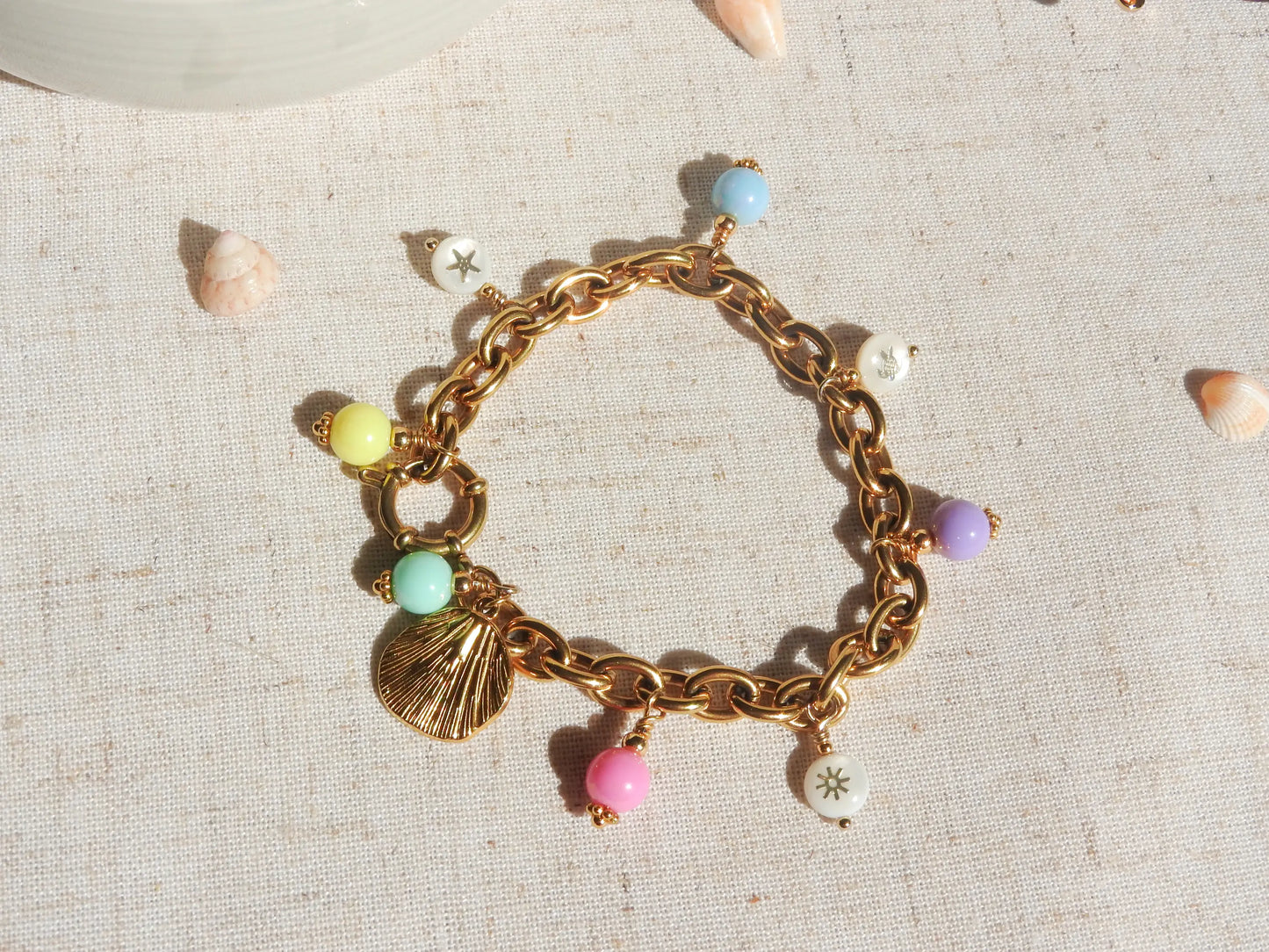 bracelet breloques à gros maillons en acier inoxydable doré. Breloques en perles colorées pastelles en acryliques, pendentif coquillage et perles en nacre blanche aux motifs étoile de mer, tortue de mer et soleil doré.