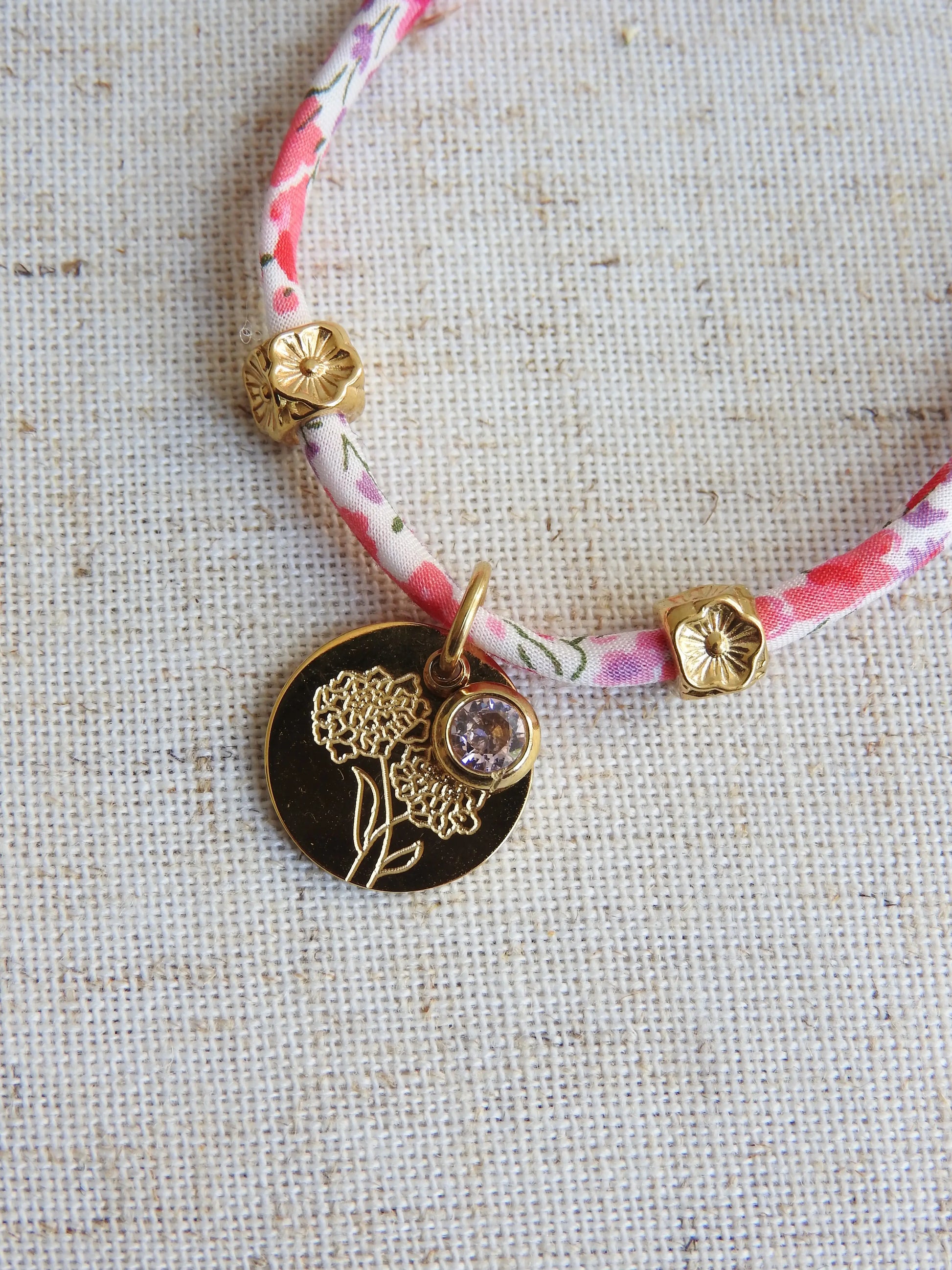 Bracelet cordon liberty Phoebe aux couleurs rose et blanc floral. Pendentif Fleur Souci et pierre quartz rose de naissance en acier inoxydable doré. Bijou zoomé sur les 2 breloques du bracelet.