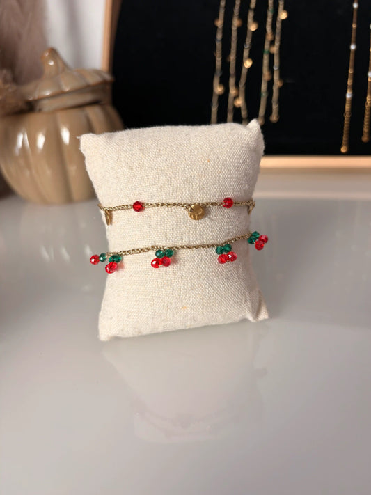 Bracelets fil crochetés à la main doré présentés sur un mini coussin en coton beige. Bracelets ornés de perles rouge et vert émeraude formant des cerises et de sequins ronds martelés en acier inoxydable doré.