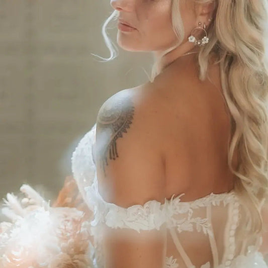 Mariée en tenue de mariage portant un bouquet de fleurs et des boucles d'oreilles Jasmine de la marque de bijoux M'Joy Creation. Bijou créoles décorées de fleur blanche en nacre et strass.