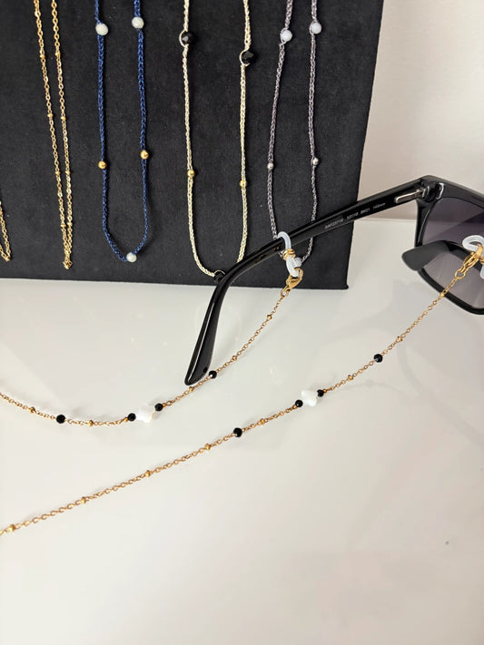 Bijou chaîne de lunettes en acier inoxydable doré et perlée, ornée de perles trèfle en nacre blanche et perles noires en verre.