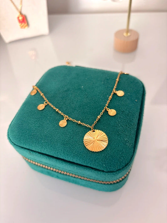 collier à pendentif rond striée et pampilles sur chaîne fine en acier inoxydable doré. Bijour présenté sur une boite à bijoux vert émeraude.