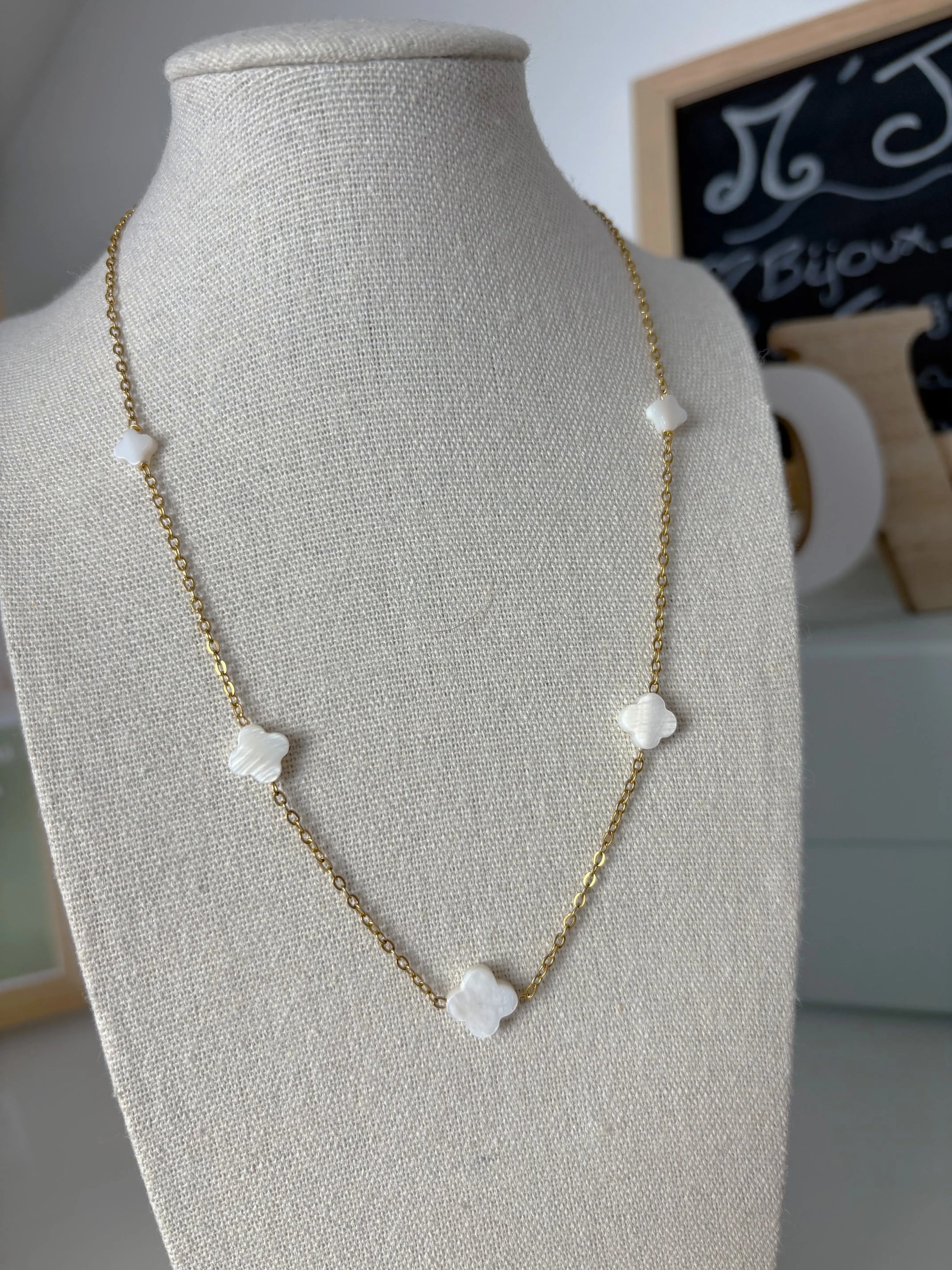 Collier chaîne fine orné de perles intercalées en forme de trèfle en nacre blanche. Bijou posé sur un buste en coton beige.