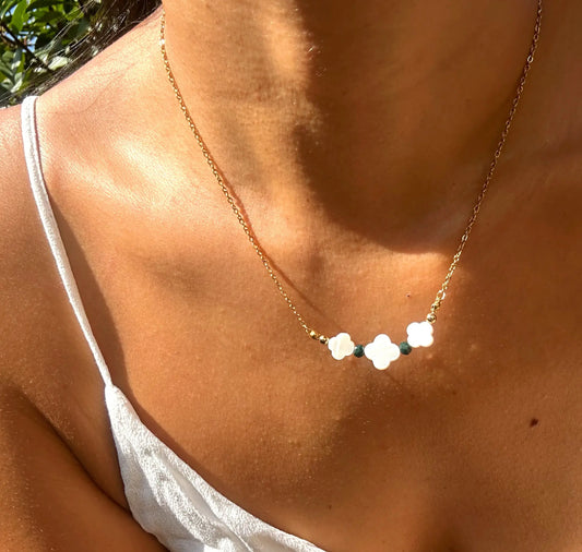 Collier chaîne en acier inoxydable doré orné de trois perles trèfle en nacre blanche et de perles de verre de couleur verte. Bijou porté sur une femme.