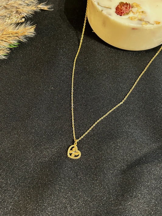 Collier à chaîne fine orné d'un pendentif coeur imbriqué d'un papillon décoré d'un strass en son centre. Bijou en acier inoxydable doré. Bijou posé sur une nappe noire décorée d'une bougie florale.