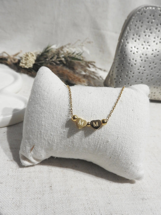 Collier chaîne fine en acier inoxydable doré, orné de deux perles plates en coeur, gravées des lettres M.