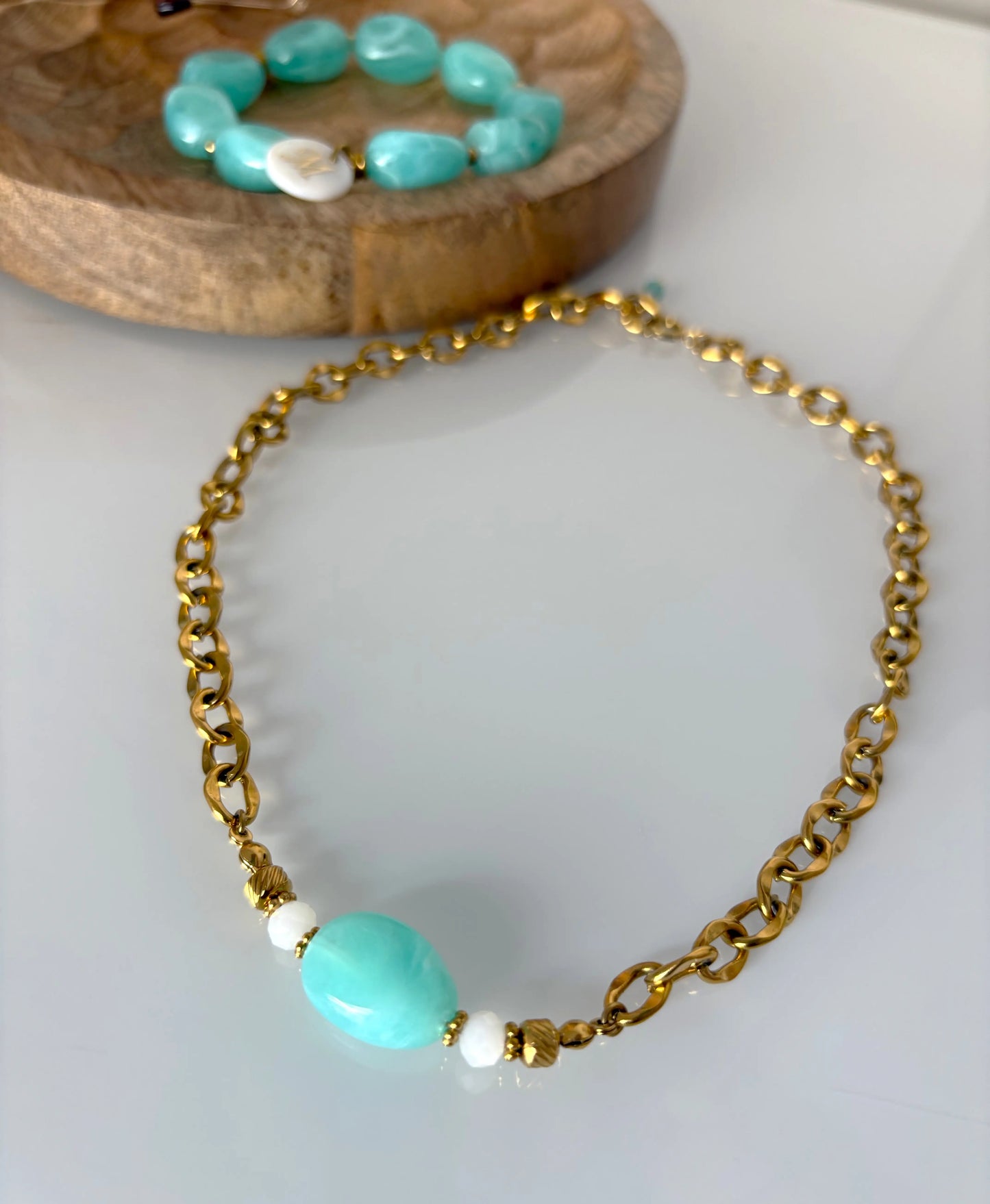 Collier chaine à larges maillons en acier inoxydable doré et orné d'une grande perle irrégulière turquoise. Bijou posé sur une table en verre trempée et en fond un bracelet de grandes perles irrégulières turquoise.