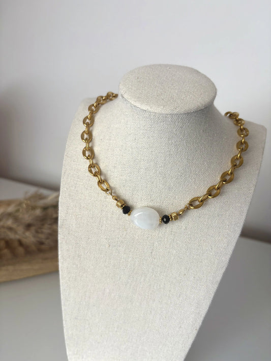 collier ras-du-cou à larges maillons en acier inoxydable doré, orné d'une grande perle irrégulière blanche marbré. Bijou présenté sur un présentoir buste beige en coton.