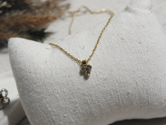 collier fine chaîne en acier inoxydable doré, orné d'un pendentif 3 pierres en oxyde de zirconium et acier inoxydable doré. Bijou posé sur un mini-coussin beige en coton.