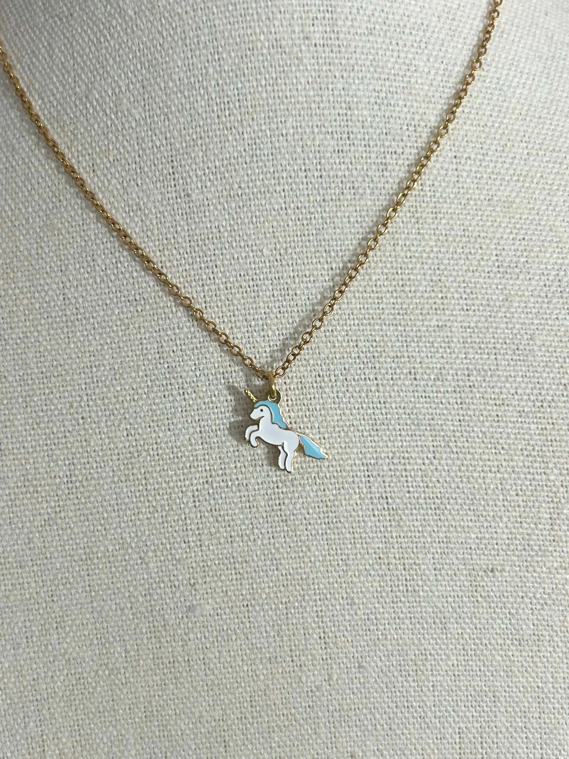 Collier pour enfant à chaîne fine posé à plat sur une nappe beige. Bijou orné d'un pendentif licorne blanche en résine époxy et acier inoxydable doré.