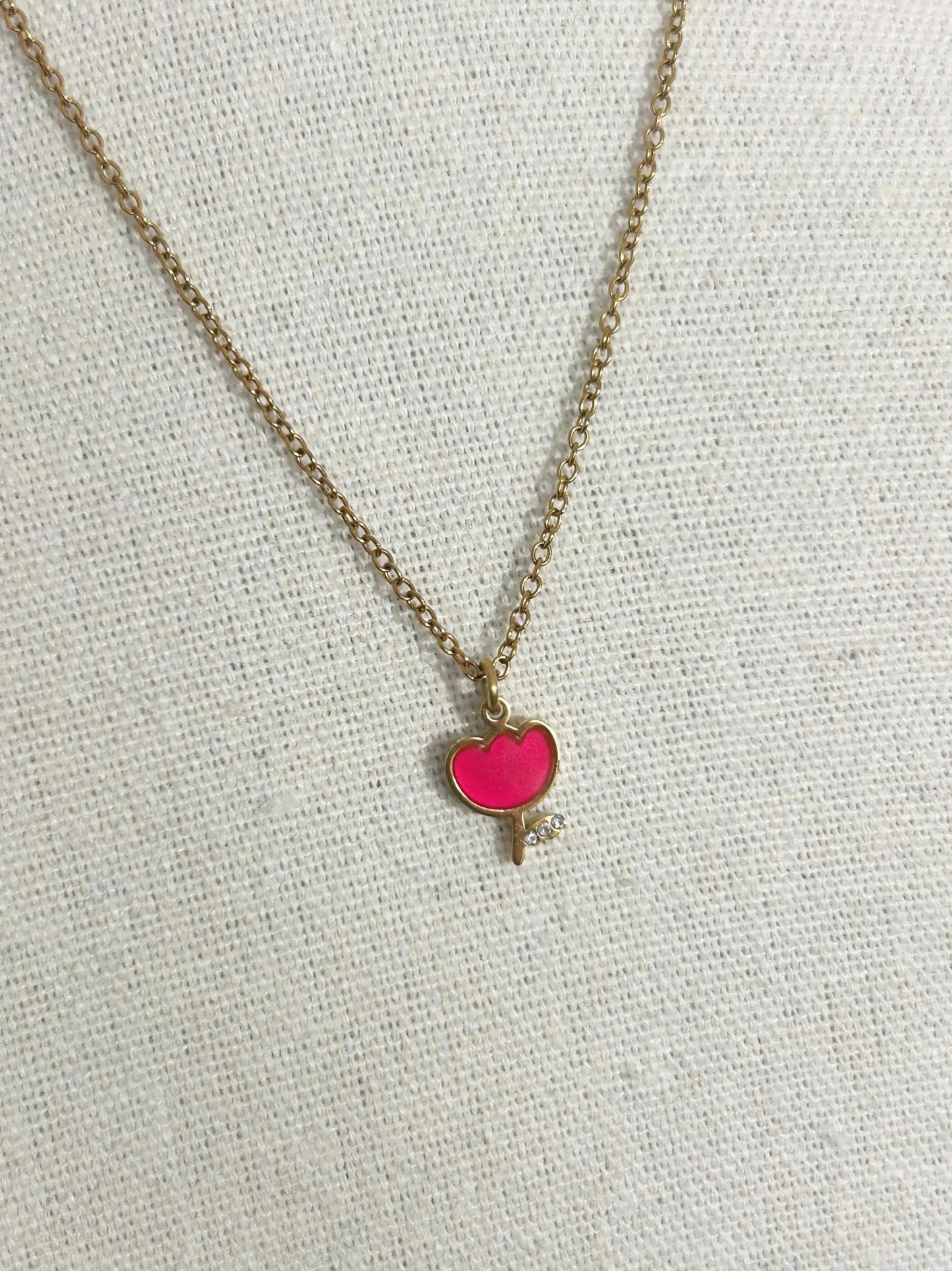 Collier pour enfant à chaîne fine posé à plat sur une nappe beige. Bijou orné d'un pendentif tulipe rouge en résine époxy et acier inoxydable doré.