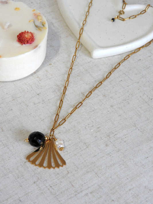 Collier sautoir en acier inoxydable doré, orné d'un pendentif en forme d'éventail doré, une perle onyx noire et une perle d'eau douce blanche.