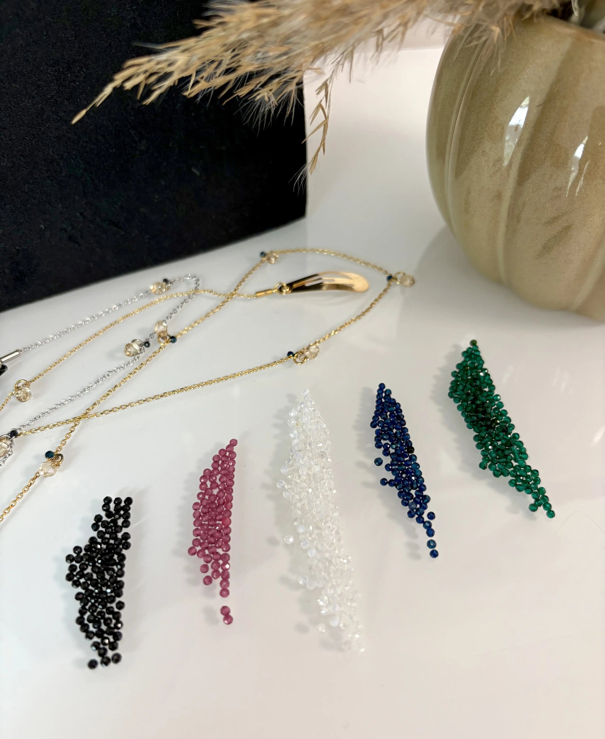 petites perles colorées noires, grenat, blanc, bleu et vert disposées sur une table en verre. Bijoux pour cheveux en acier inoxydable avec barrette dorée et chaîne en acier inoxydable.