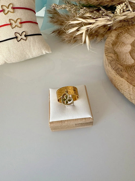 bague à anneau martelé réglable en acier inoxydable doré et ornée d'une breloque coeur papillon strass en breloque. Bijou posé sur un support en bambou, posé sur une table en verre.