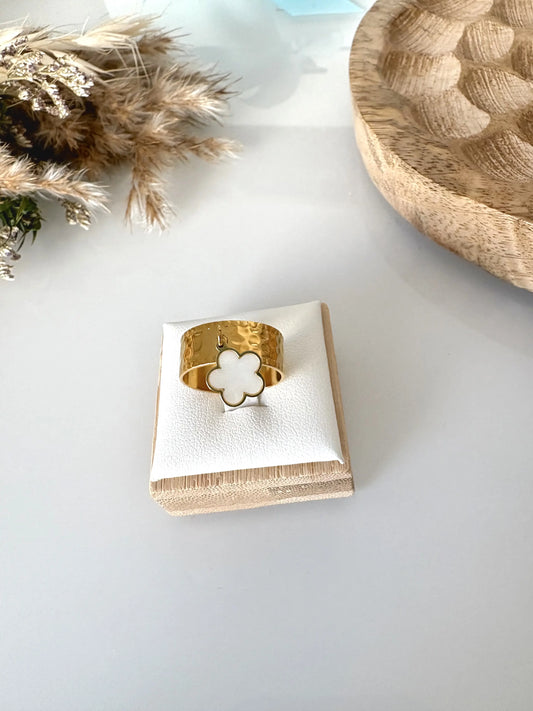 bague anneau martelé réglable en acier inoxydable doré, breloque fleur en nacre blanche. Bijou posé sur un support en bambou, sur une table en verre décorée d'un plateau bambou et un mini-bouquet.