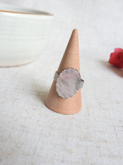 bague à anneau réglable en acier inoxydable argenté posée sur un cône en bambou. Bijou orné d'une pierre plate naturelle en quartz rose. 