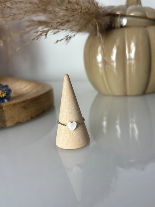 bague chaîne en acier inoxydable argenté et ornée d'une perle coeur en nacre blanche. Bijou présenté sur un cône en bambou, posé sur une table en verre trempée et décorée d'un bol en citrouille kaki et un plateau en bambou.