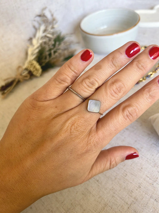 Bague chaîne en acier inoxydable doré portée au majeur. Bijou orné d'une perle carré en nacre aux reflets noir, gris et blanc.