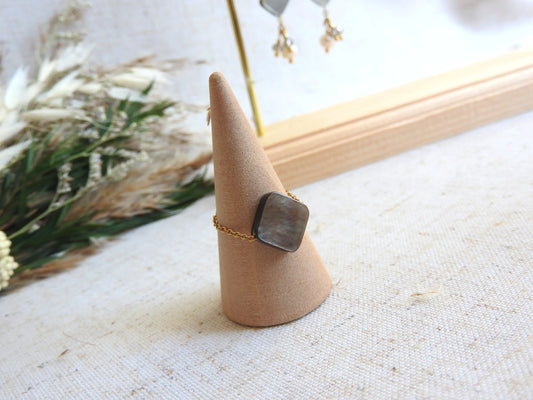 bague chaînette en acier inoxydable doré, ornée d'une perle en nacre aux reflets noirs irisés et posée sur un cône en bambou
