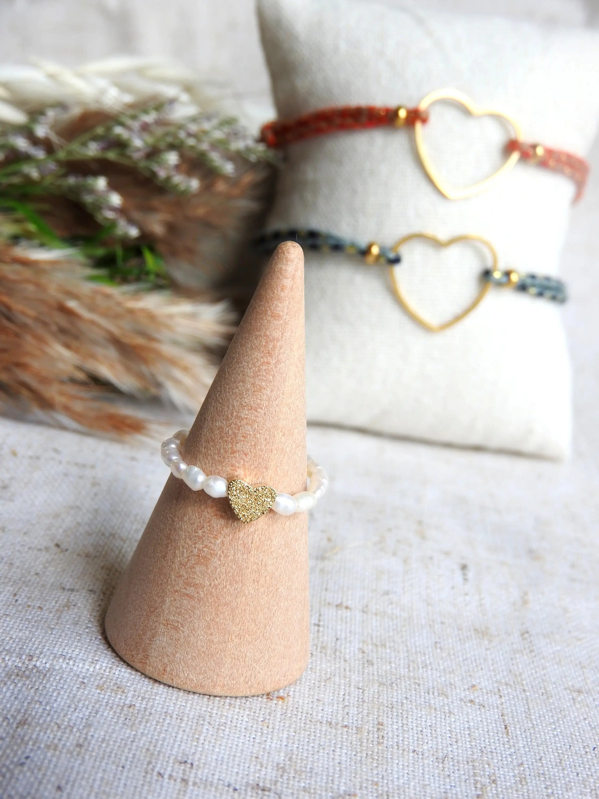 Bague élastique en perles d'eau douce blanche et perle cœur à effet diamanté en acier inoxydable doré. Bijou posé sur un cône en bambou. 