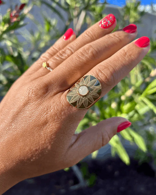 bague style bohème, ethnique réglable en acier inoxydable doré, ornée d'une pierre de lune, portée à l'index sur fond de végétations.