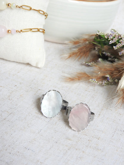 bagues à anneau réglable en acier inoxydable argenté posées à plat sur une nappe beige décorée d'un mini-bouquet de fleurs. Bijoux ornés de piettes naturelles, une pierre plate en nacre blanche et une pierre en quartz rose. 