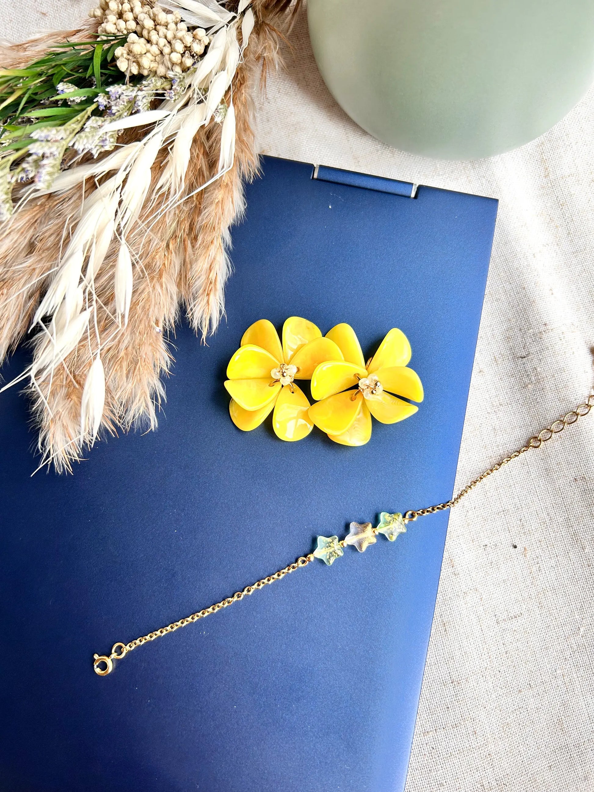 Suspensions pour créoles en acier inoxydable assemblées à la main. Bouquet floral réalisé à partir de pétales en acrylique jaune et de perles de verre colorées et en acier inoxydable doré. Bijou posé sur le dessus d'un ordinateur portable avec un bracelet chaîne fine orné de perles en forme d'étoile scintillante de couleur vert pomme.