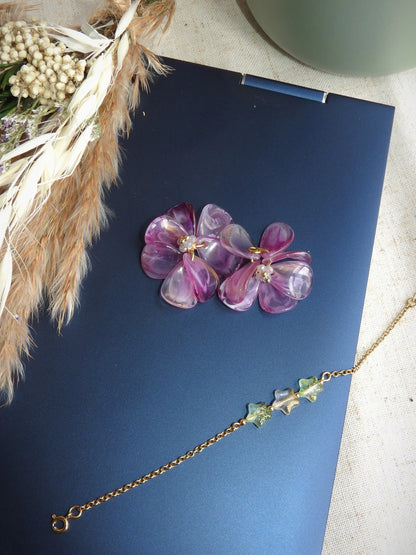 Suspensions pour créoles en acier inoxydable assemblées à la main. Bouquet floral réalisé à partir de pétales en acrylique violet marbré et de perles de verre colorées et en acier inoxydable doré. Bijou posé sur le dessus d'un ordinateur portable avec un bracelet chaîne orné de perles en forme d'étoile scintillante couleur vert pomme.