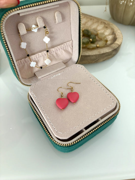 boite à bijoux dans laquelle sont disposées un bracelet chaine et perles de noires et trèfle en nacre blanche, ainsi que paire de boucles d'oreilles crochet en acier inoxydable doré avec une perle coeur couleur hibiscus.