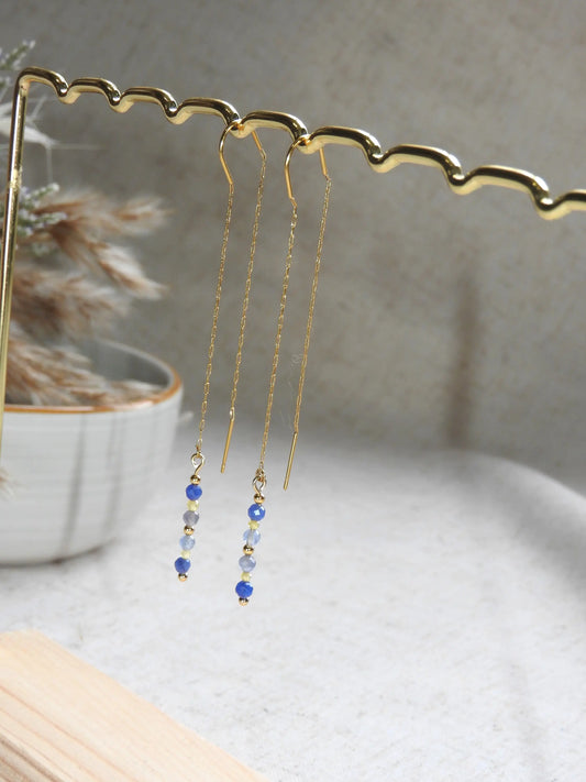 boucles d'oreilles à chaînette traversante en acier inoxydable doré, suspendue sur une barre métallique doré et bambou. Bijou orné de perles de verre de tons bleus et jaune.