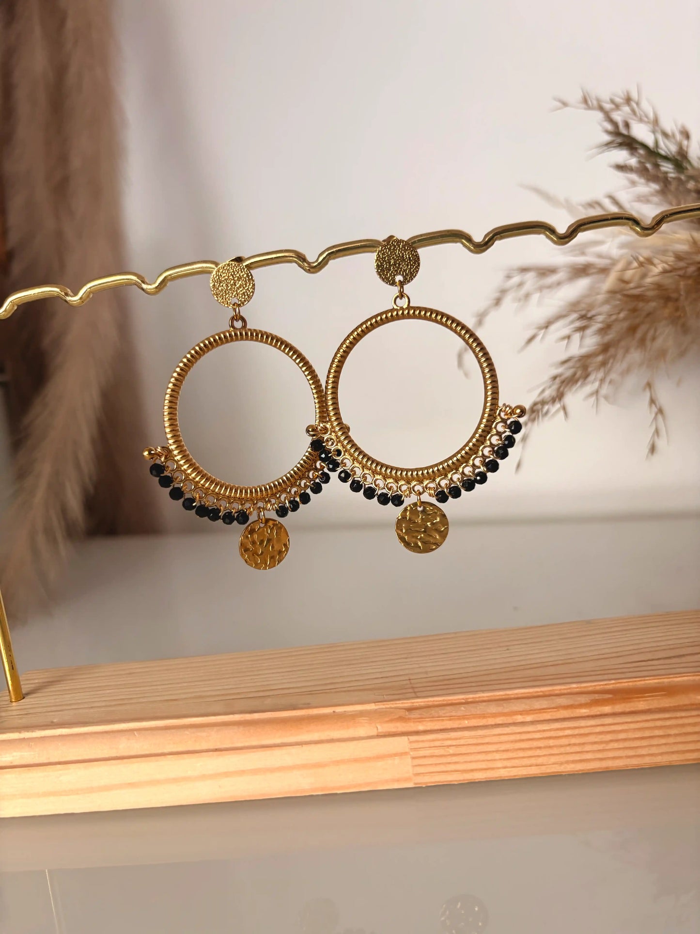 boucles d'oreilles chandelier en acier inoxydable doré et orné de perles noires et de sequins rond martelé. Bijoux présentés sur un support métallique doré et bambou.