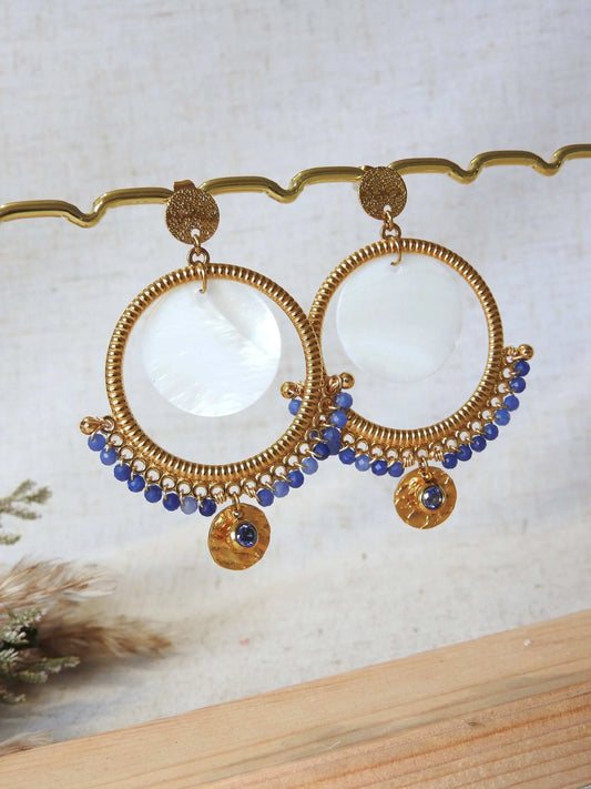 boucles d'oreilles clous à disque martelé ornées d'un chandelier décoré d'un double sequin en nacre blanche et acier inoxydable doré et des perles de verre bleu en décoration. Finition de la boucle avec une pierre de naissance saphir pour le mois de septembre. Bijoux suspendus à une barre métallique doré.