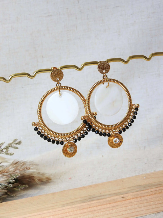 boucles d'oreilles clous à disque martelé ornées d'un chandelier décoré d'un double sequin en nacre blanche et acier inoxydable doré et des perles de verre noires en décoration. Finition de la boucle avec une pierre de naissance cristal pour le mois d'avril. Bijoux suspendus à une barre métallique doré.