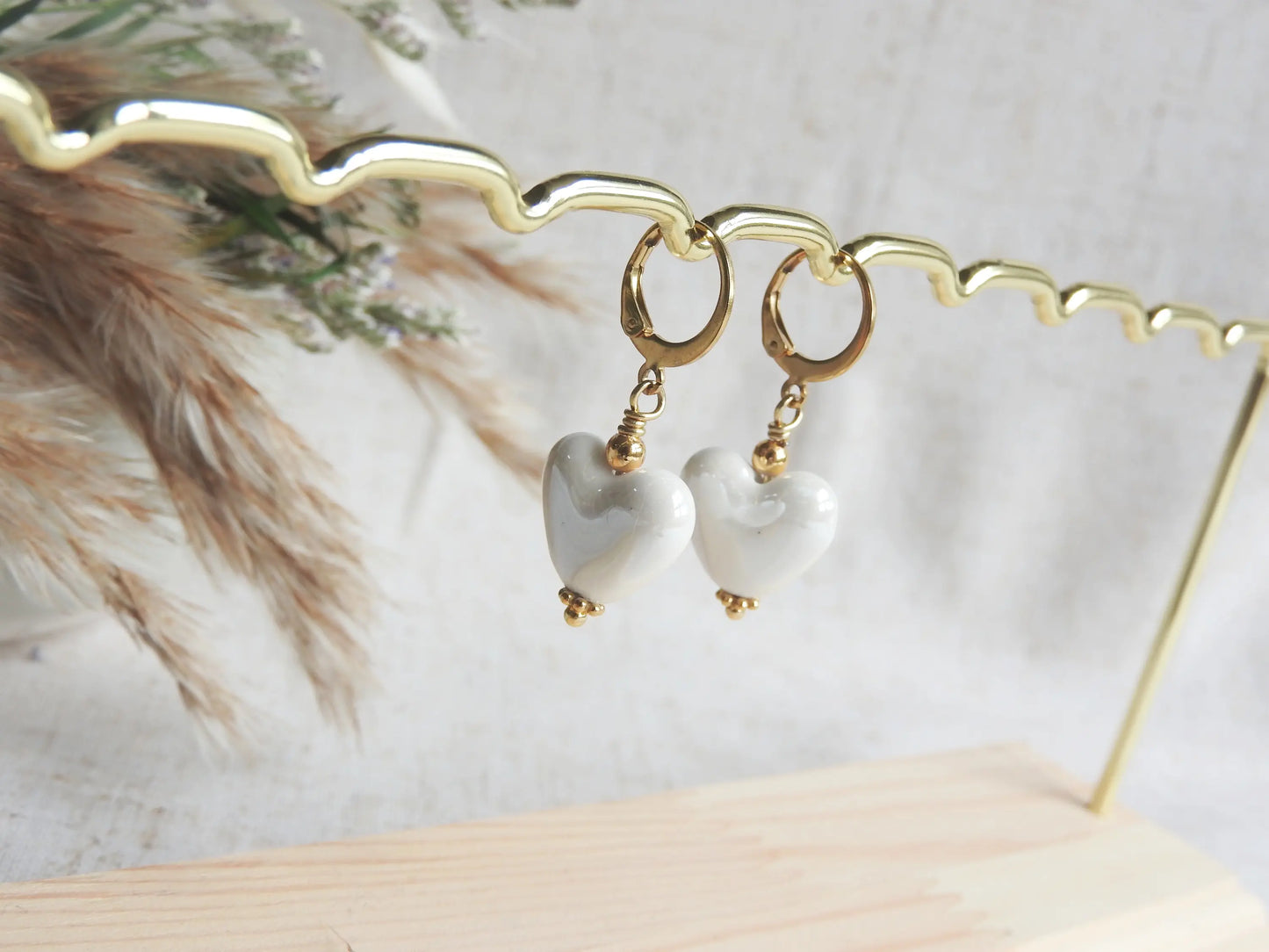 Boucles d'oreilles dormeuses créoles en acier inoxydable doré, décorées d'une perle cœur en céramique blanche. Bijou suspendu sur un support métallique doré et bambou.