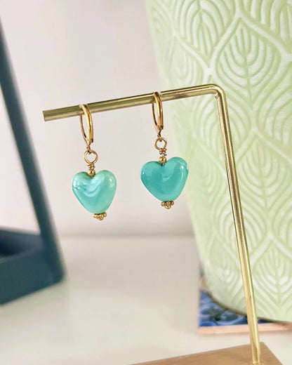 Boucles d'oreilles dormeuses créoles en acier inoxydable doré, décorées d'une perle cœur en céramique turquoise. Bijou suspendu sur un support métallique doré et bambou.