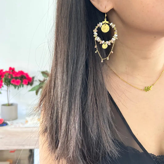 Boucles d'oreilles crochets avec créoles décorées de perles de verre couleur blanc, sable et jaune qui font tout le tour de la créole et sequins martelés, chaînette pendantes. Bijou en acier inoxydable doré, porté par une femme aux longs cheveux noirs.