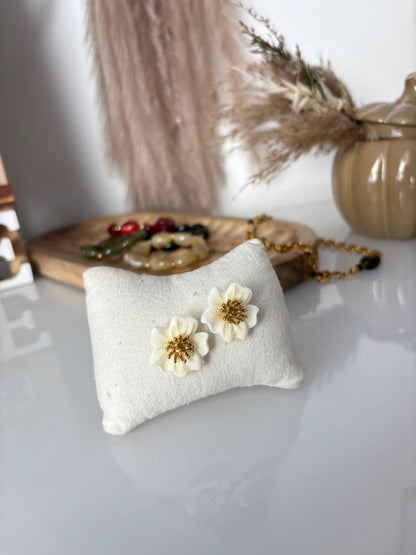 boucles d'oreilles tiges pistil en acier inoxydable doré et fleur hibiscus couleur crème. Bijoux présentés sur un mini-coussin en coton beige