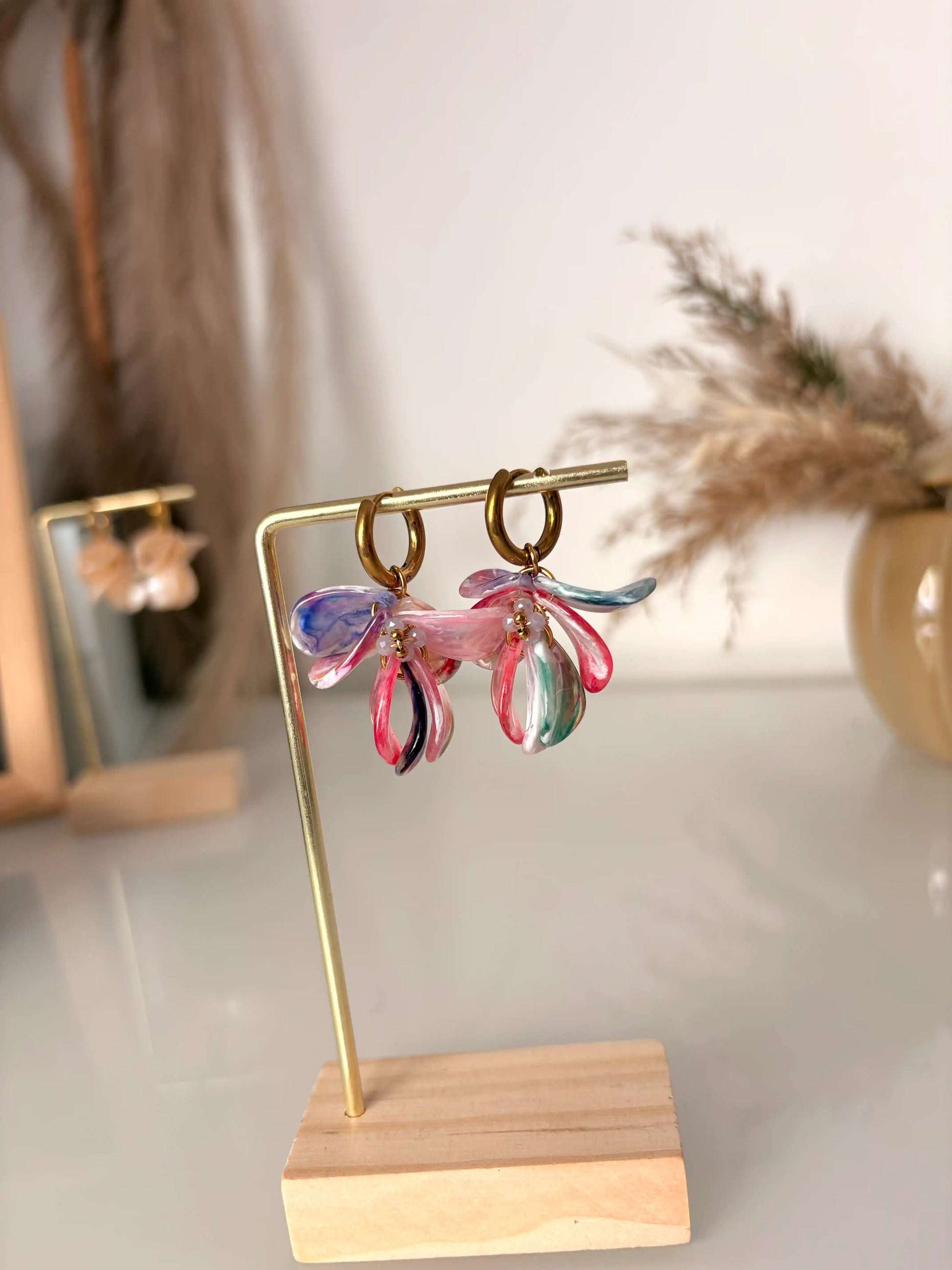boucles d'oreilles mini-créoles en acier inoxydable doré et décorées de pétales sequins multicouleurs et perles de verre lilas. Bijoux présentés sur un support métallique doré et bambou.